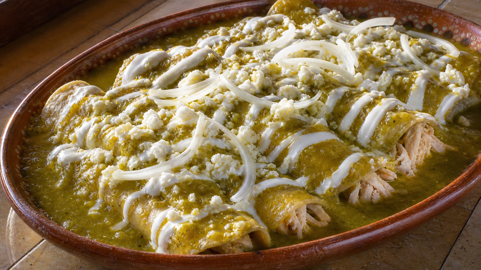 Enchiladas verdes mexicanas rellenas de pollo, bañadas en salsa de tomatillo y decoradas con crema, queso fresco y cebolla